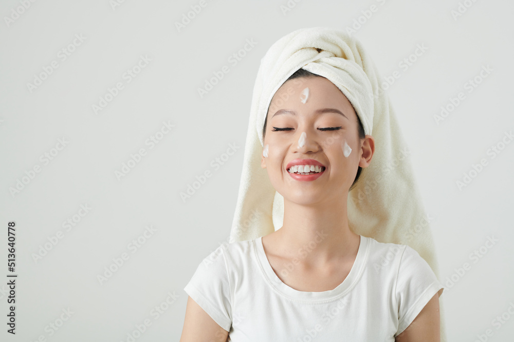 Portrait of happy young Asian woman applying moisturizing face cream after shower Portrait of happy young Asian woman applying moisturizing face cream after shower