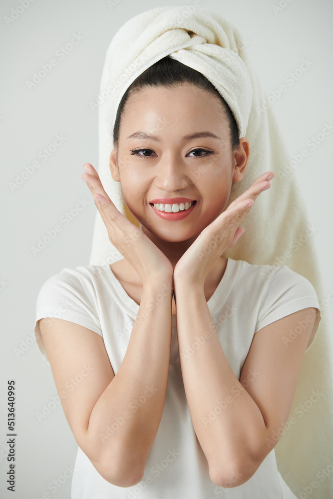 Cheerful young woman with towel on head touching her fresh glowy skin Cheerful young woman with towel on head touching her fresh glowy skin