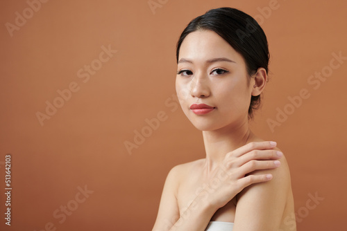 Serious young woman wrapped in towel touching shoulder and looking at camera