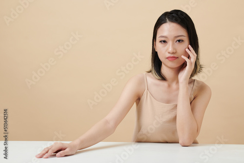 Portrait of serious confident young woman touching face and looking at camera