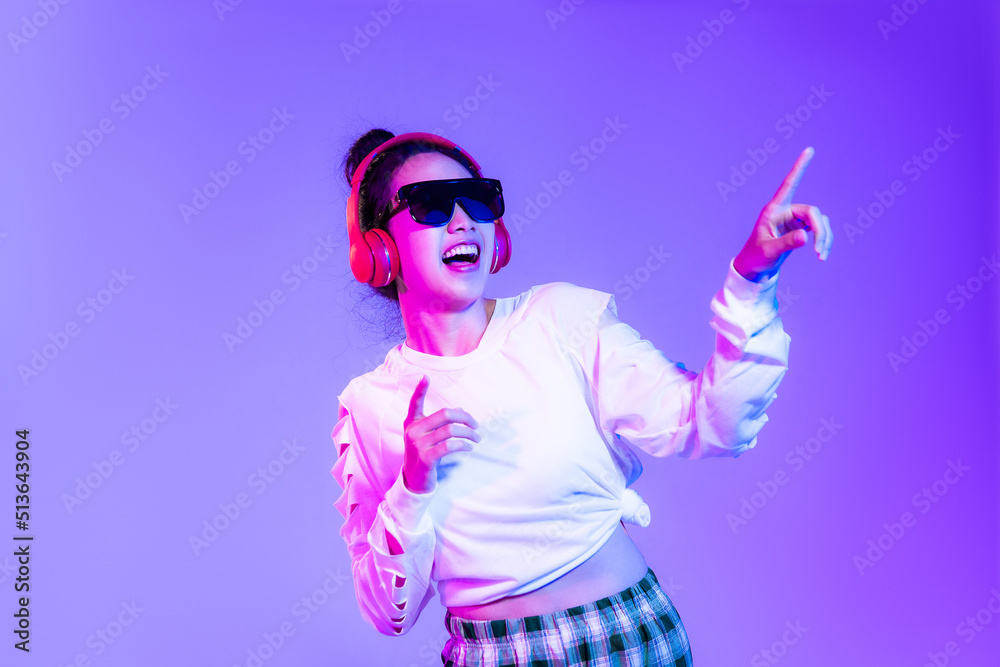 Young asian woman in white fashion crop sweatshirt wearing sunglasses and red headphones listen to music dancing and finger pointing on the purple background.
Young asian woman in white fashion crop sweatshirt wearing sunglasses and red headphones listen to music dancing and finger pointing on the purple background.