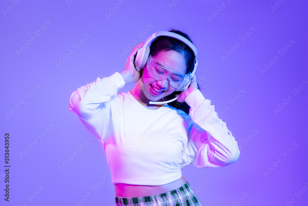 Young asian woman in white shirt wearing headphones posing on blue and purple background.
Young asian woman in white shirt wearing headphones posing on blue and purple background.