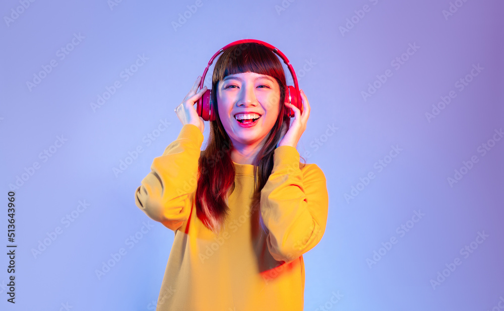 Young asian woman in yellow sweatshirt wearing red headphones smiling and listen to music on the purple screen background.
Young asian woman in yellow sweatshirt wearing red headphones smiling and listen to music on the purple screen background.