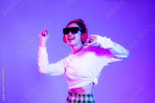 asian woman in white fashion crop sweatshirt wearing sunglasses and red headphones listen to music and dancing isolated purple background.