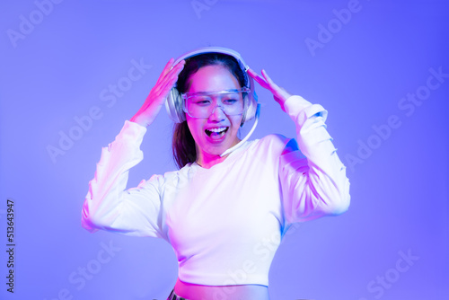 Young asian woman in white shirt wearing headphones posing dancing on blue and purple background. 