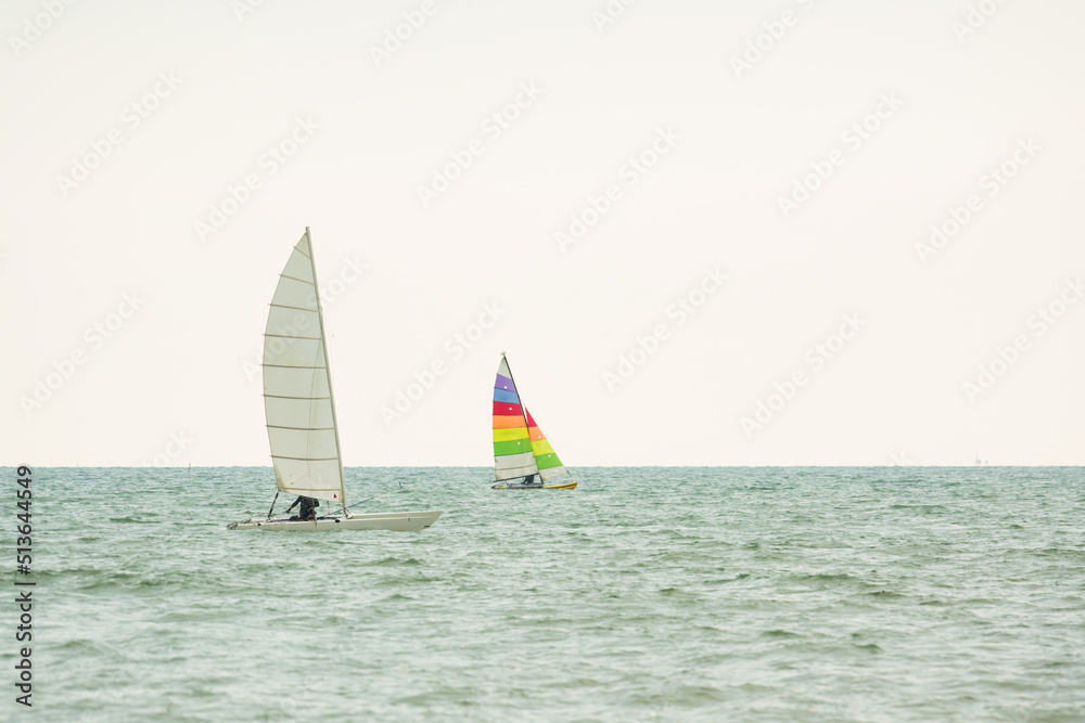 Sailboat in the sea on white sky background.Luxury summer adventure and active vacation in the ocean.Sport sailboat sailing through a silver sea in a sunny day. Sailboat in the sea on white sky background.Luxury summer adventure and active vacation in the ocean.Sport sailboat sailing through a silver sea in a sunny day.