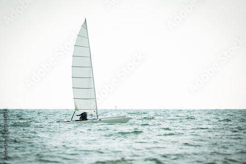 Sailboat in the sea on white sky background.Luxury summer adventure and active vacation in the ocean.Sport sailboat sailing through a silver sea in a sunny day.