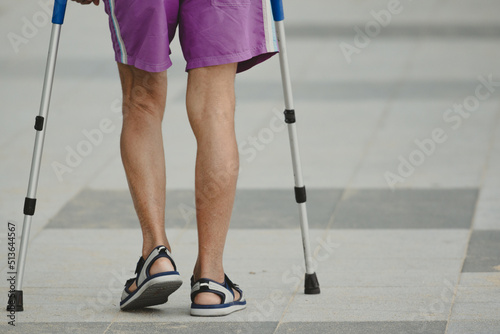Disable man using crutches to walk for rehab.Patient with leg injury during training with crutches.Old man walking on the street for outdoor exercise.