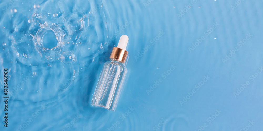 Naklejka premium Glass bottle of anti aging serum and falling water drops on blue background. Facial serum mockup. Copy space.