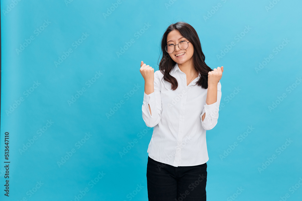 Overjoyed cute Asian businesswoman in round glasses classic office dress code celebrates successful project posing isolated on blue studio background. Cool business offer. Work Life Balance concept Overjoyed cute Asian businesswoman in round glasses classic office dress code celebrates successful project posing isolated on blue studio background. Cool business offer. Work Life Balance concept