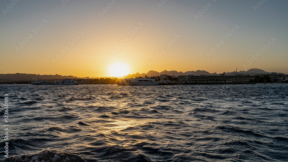 Fototapeta premium Sunset over the Red Sea. The sun is low. Silhouette of a mountain range against an orange sky. Ripples and highlights on the water. Egypt. Safaga