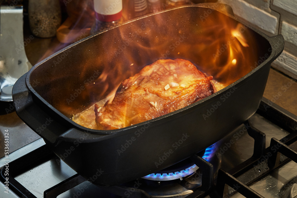 Piece of beef meat, fried with onions in wine sauce in rectangular pan on gas stove fire. Flombe French gourmet cuisine Piece of beef meat, fried with onions in wine sauce in rectangular pan on gas stove fire. Flombe French gourmet cuisine