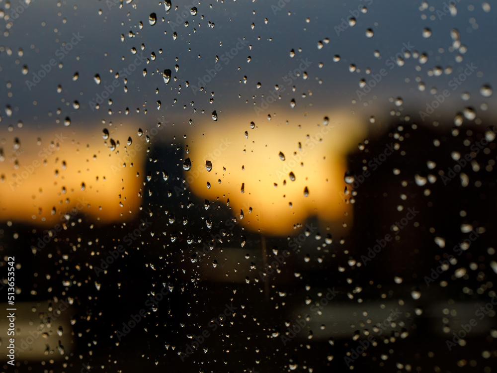Close up and macro view of raining water drop on clear transparent glass and blur background of silhouette landscape, sun with golden light durning sunset or sunrise.