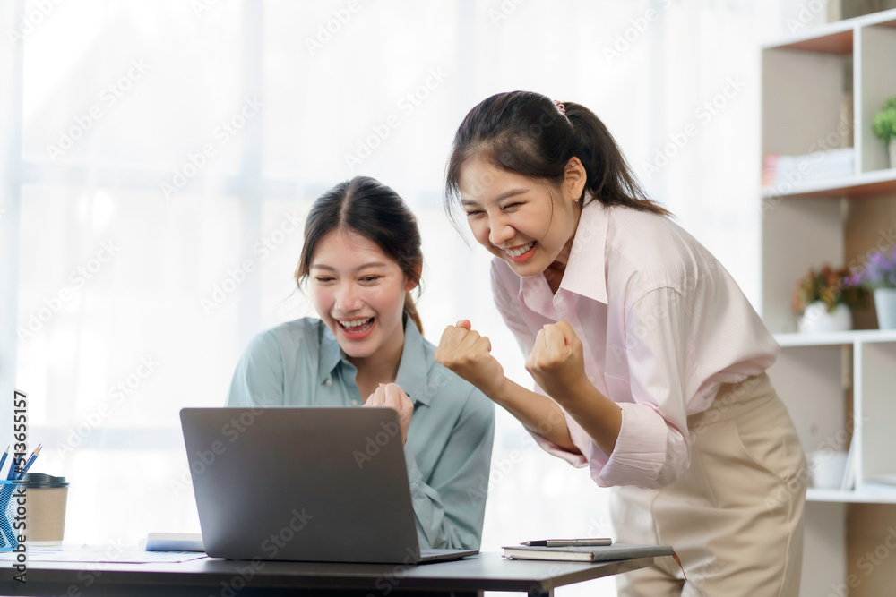 Happy two young Asian businesswomen successful excited raised hands rejoicing with laptop computer in office. New startup project concept. Happy two young Asian businesswomen successful excited raised hands rejoicing with laptop computer in office. New startup project concept.