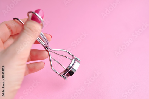 Steel curler for eyelashes on hand on pink background