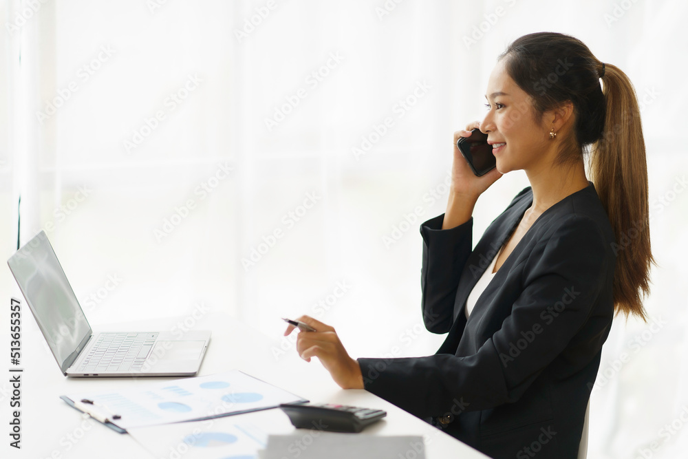 Happy young Asian business woman sitting smiling and talking on mobile phone in office. Happy young Asian business woman sitting smiling and talking on mobile phone in office.