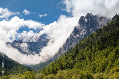 Close up on the mountains in Daocheng Yading Nature Reserve in dense white clouds, horizontal image with copy space for text, blue sky, sunny day