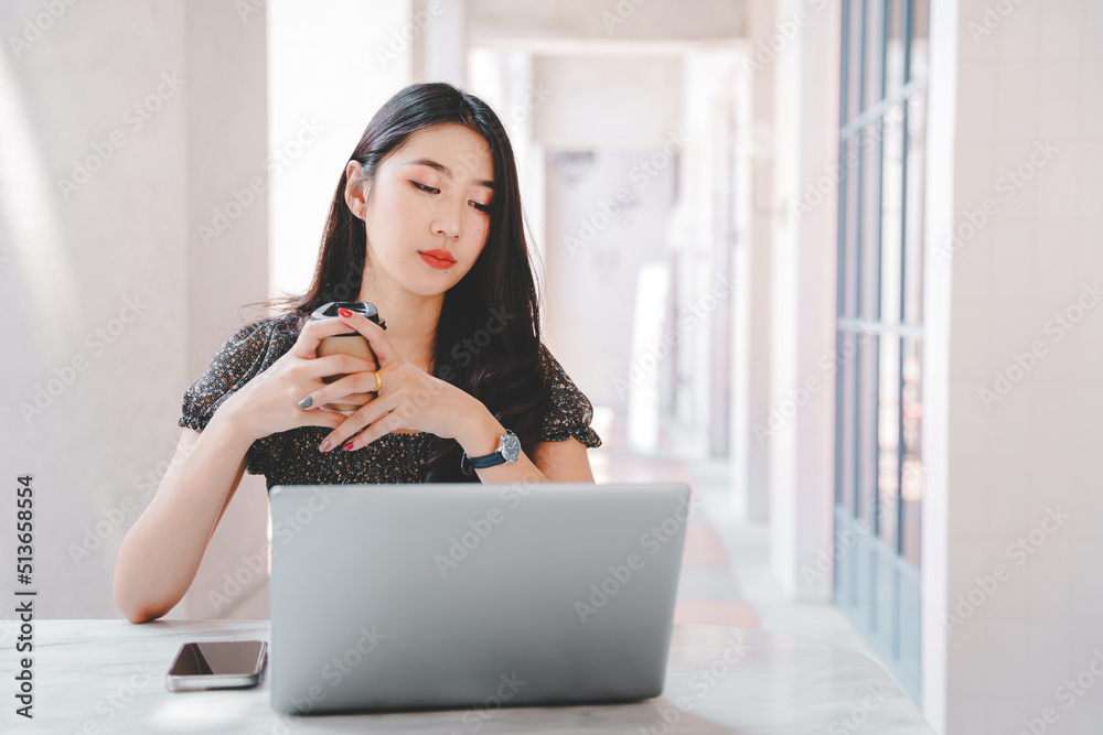 Beautiful Asian girl enjoys coffee while working in a coffee shop on laptop connected to public wifi. Stylish college student studying online while spending free time in the park. Beautiful Asian girl enjoys coffee while working in a coffee shop on laptop connected to public wifi. Stylish college student studying online while spending free time in the park.