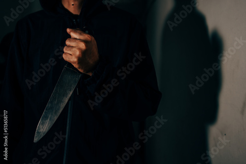 The image of a male murderer holding a knife in a dark room is terrifying as he is about to attack the victim. photo