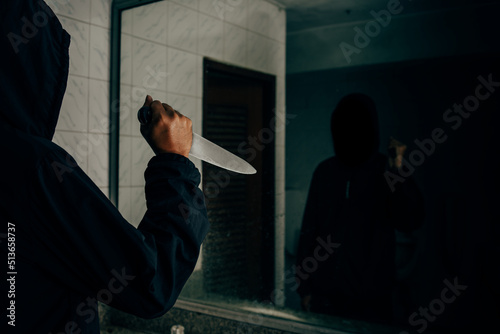 Rear view of a murderer holding a knife In the bathroom, he was looking at himself in the mirror.
