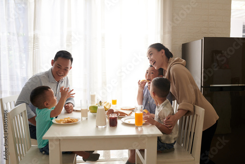 Happy joyful Asian family of five eating tasty breakfast at kitchen table