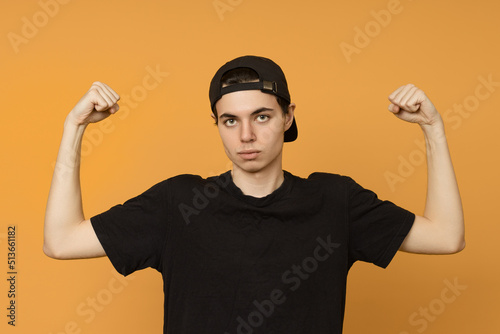 student in a black t-shirt and cap shows strong hands on a yellow background