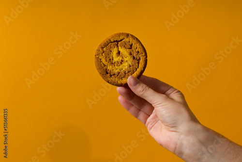 sweet biscuit in human hand close up on yellow background