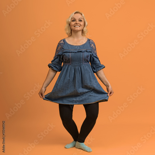 Fotografie, Obraz pretty blond bbw woman in a blue dress makes a curtsey on a colored background