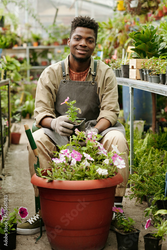 Photography Portrait of African young gardener smiling at camera while sitting in flower sho