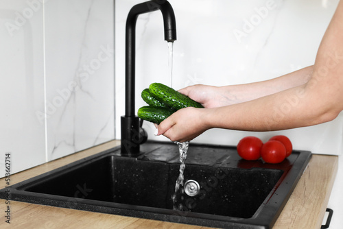 A woman's hands wash cucumbers and tomatoes under a stream of water in the kitchen. Clean vegetables and a healthy lifestyle