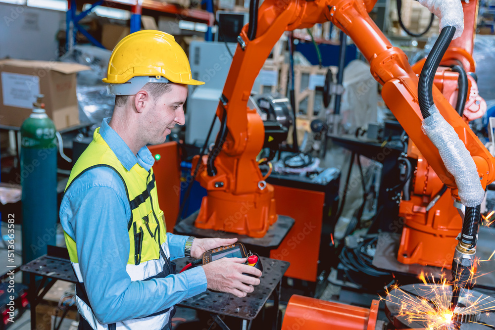 Worker man working with robot arm automate welding machine in modern metal factory. Engineer program robotic in heavy industry.