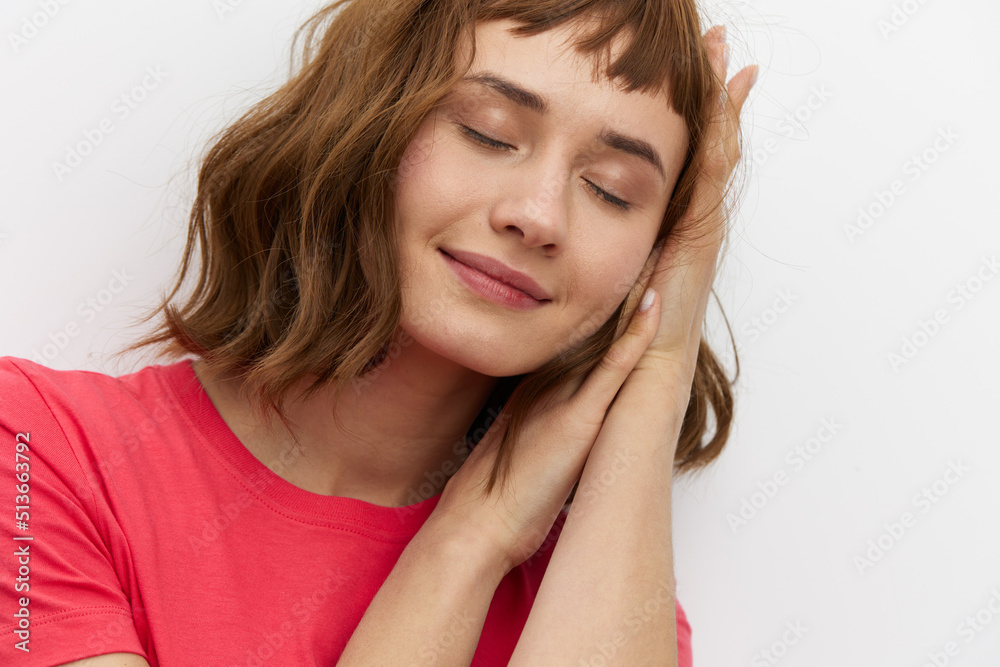 a gentle, relaxed, sleepy woman stands in a red T-shirt on a white background and holds her hands folded in her palms under her head, closing her eyes a gentle, relaxed, sleepy woman stands in a red T-shirt on a white background and holds her hands folded in her palms under her head, closing her eyes