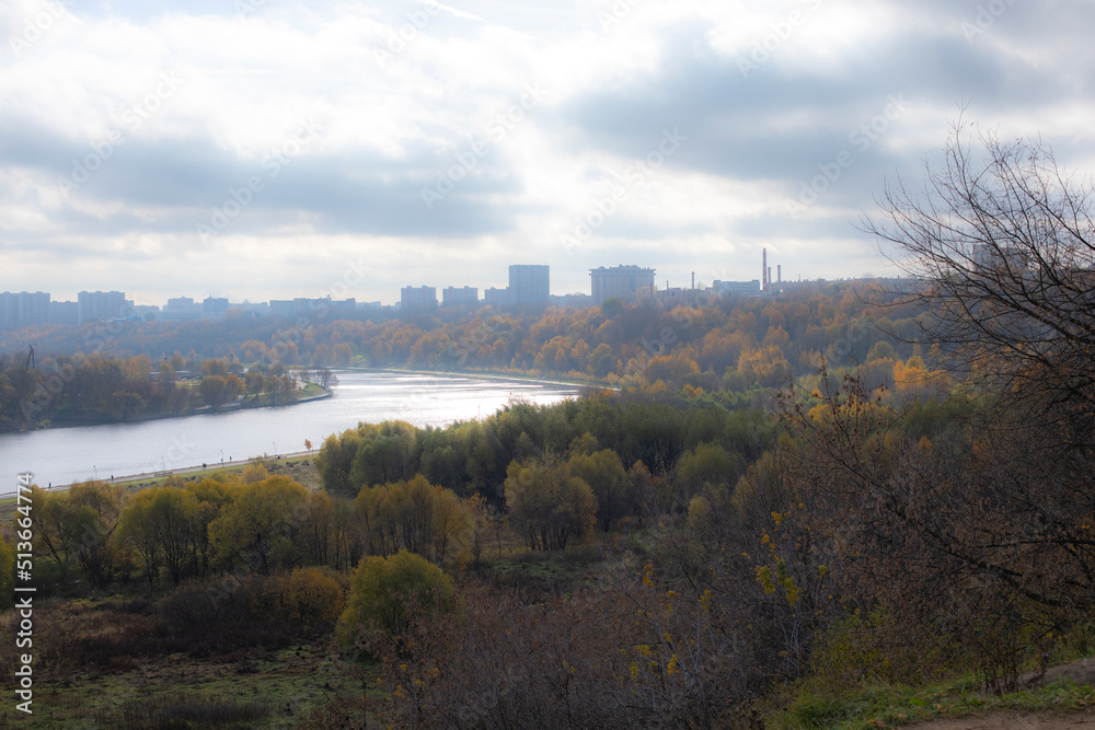 Obraz premium City park in autumn, river bend, yellowing deciduous trees and high-rise residential buildings, photo defocus soft focus