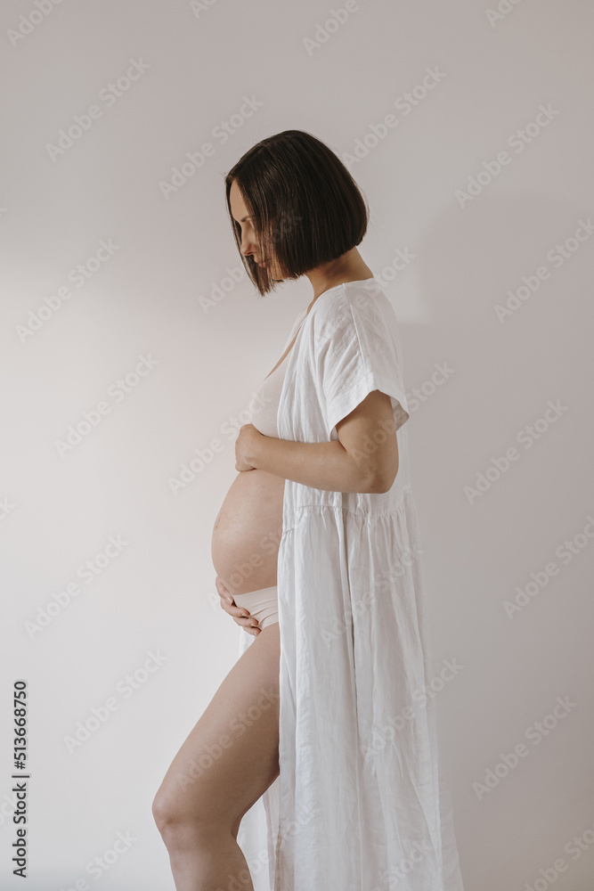 Young pregnant woman stays near white wall. Pregnancy, motherhood, maternity concept. Happy pregnant woman with big belly Young pregnant woman stays near white wall. Pregnancy, motherhood, maternity concept. Happy pregnant woman with big belly