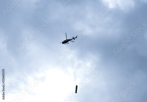 A silhouette picture with noise effect of fast moving and motion blur helocopter carrying things at the sky.