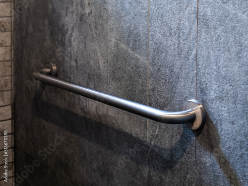 Close-up photo of stainless steel grab bar handrail installed on grey stone tiles wall background in a hotel handicapped disabled access bathroom. photo