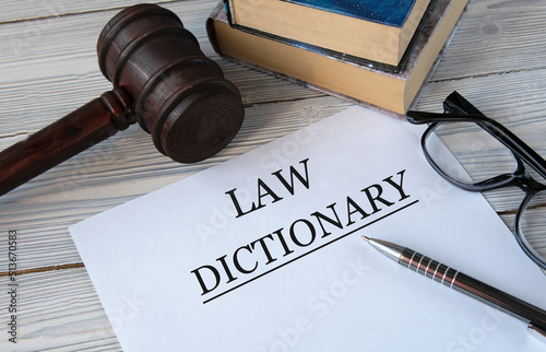 LAW DICTIONARY - words on white paper with the background of the judge's hammer, glasses and pen