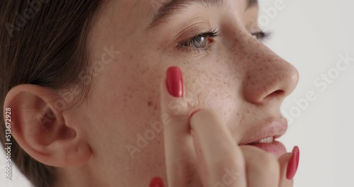 Woman with freckles on soft well-groomed skin applying moisturising cream and smiling
