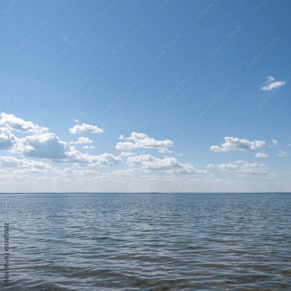 View of a beautiful large lake that merges with the blue bright summer sky. Sunny summer day relaxing on the lake