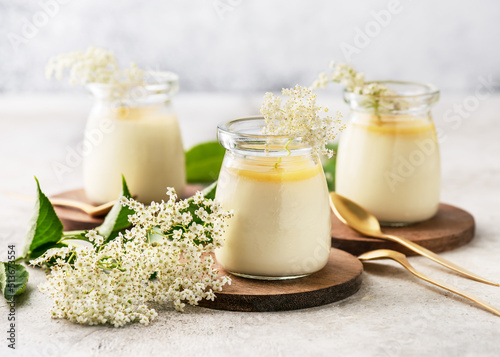 Homemade creamy elder flowers panna cotta with lemon sauce in vintage glass jars on a light concrete background. Desserts without baking.  photo