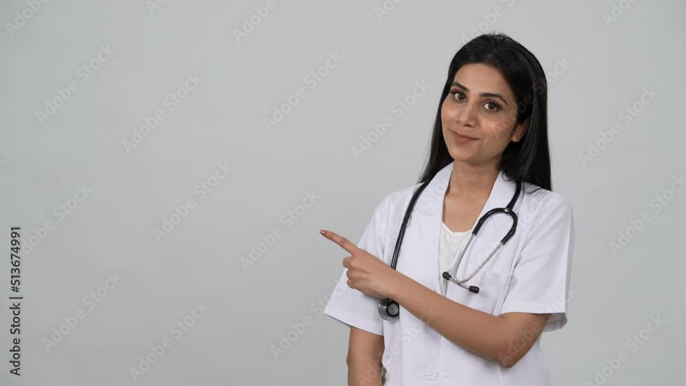 A young Indian woman wearing white medical coat and stethoscope and indication out side.Smiling Asian female physician posing in studio.