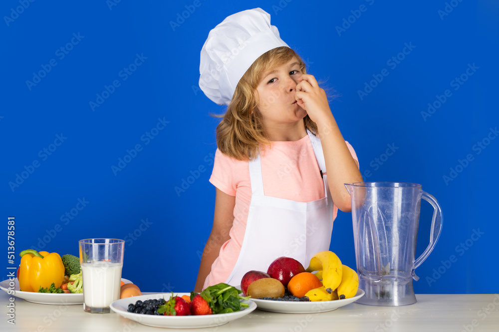 Fruits and vegetables for kids. Child wearing cooker uniform and chef hat preparing vegetables on kitchen, studio portrait. Cooking, culinary and kids food concept. Fruits and vegetables for kids. Child wearing cooker uniform and chef hat preparing vegetables on kitchen, studio portrait. Cooking, culinary and kids food concept.