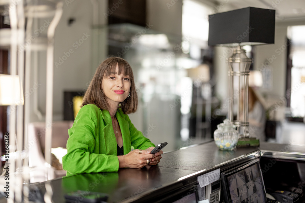 Young stylish business woman stands with phone on reception of luxury hotel. Woman check in hotel during a business trip