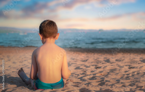 Boy sits back and looks out at sunset at sea, lifestyle, seaside holiday, space for text.