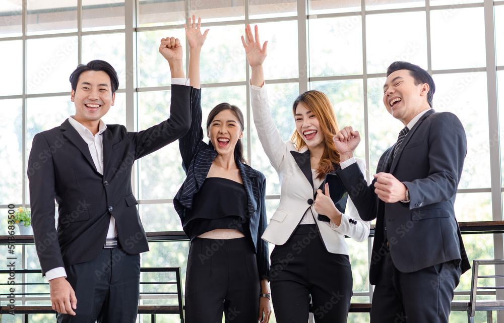 Group of Asian young happy cheerful millennial professional successful male businessman female businesswoman employee colleague in formal suit standing smiling holding fists up celebrating together