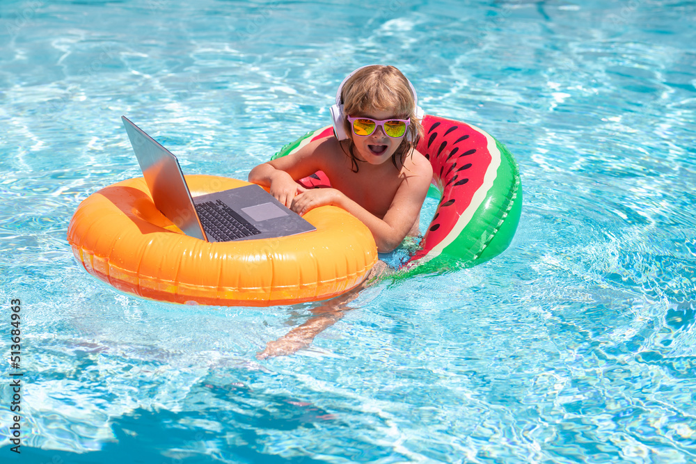 Business and summer. Kid remote working on laptop in pool. Little business man working online on laptop in summer swimming pool water.