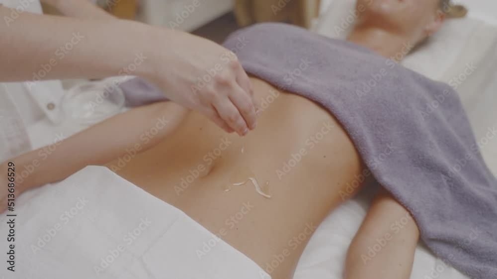 Masseuse drips oil on stomach and rub it to skin circular movements of hands. Masseuse drips oil on stomach and rub it to skin circular movements of hands.