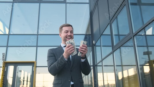 Happy successful young businessman counts, flaunts, cash on the background of a modern office