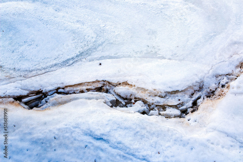 Cracks on thick ice on surface of frozen river in winter season, powdered by snow and sand, with brilliant snow and ice crystals.