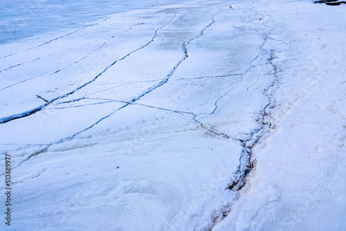 Cracks on thick ice on surface of  frozen river in winter season, powdered by snow and sand, with brilliant snow and ice crystals. photo